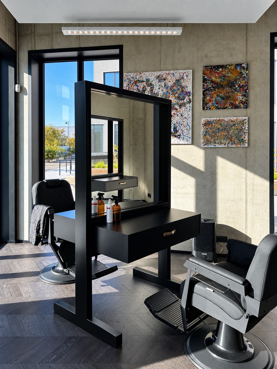 Men’s Studio päikeseline salong: mustad juuksuritoolid ja peegel, betoonseinal värvilised maalid