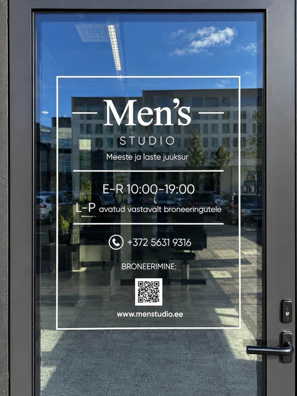 Otsevaade Men’s Studio klaasuksele: valge logokleebis, lahtiolekuajad ja broneerimise QR-kood